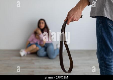 Concept de violence domestique. Femme effrayée embrassant et couvrant la fille tout en colère homme tenant la ceinture dans les mains Banque D'Images