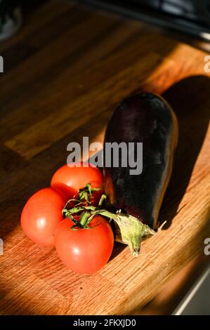 Tomates sur la vigne et une aubergine fraîche (aubergine) Solanum melongena sur une planche à découper en bois Banque D'Images