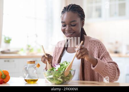 Concept de nutrition saine. Happy Black Femme cuisine salade de légumes frais dans la cuisine Banque D'Images