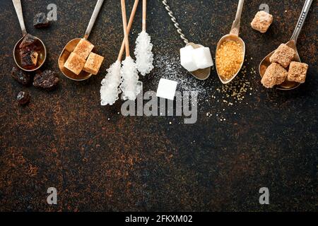 Sucre blanc, cubes de sucre de canne, caramel en cuillères à café sur fond de béton de table brun foncé. Différents types de sucre assortis. Vue de dessus ou plan de travail. Banque D'Images