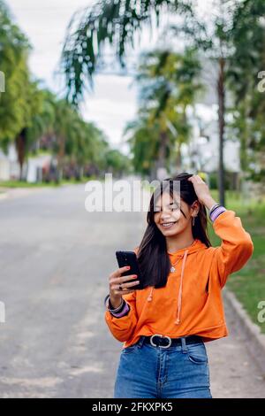 Bonne fille hispanique de l'adolescence regardant le téléphone intelligent Banque D'Images