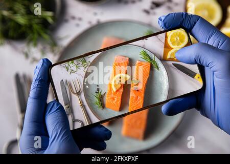 Homme avec des gants prenant des photos de nourriture sur table Banque D'Images