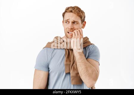 Image de l'homme anxieux de tête rouge piquant les ongles de doigt et regardant à gauche avec peur visage inquiet, regardant quelque chose avec l'anxiété, se tenant nerveux Banque D'Images