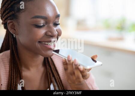 Jeune femme noire souriante utilisant l'option Virtual Voice Assistant activée Smartphone Banque D'Images