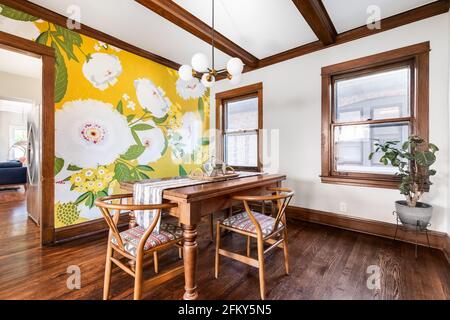 Une salle à manger avec un éclairage moderne suspendu au plafond. Un papier peint aux fleurs vibrantes est sur le mur lointain avec des poutres en bois foncé sur le plafond. Banque D'Images