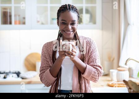 Détente à la maison. Portrait d'une femme africaine heureuse buvant du café du matin dans la cuisine Banque D'Images