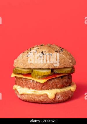 Hamburger végétalien maison avec patty de soja, fromage à la noix de cajou et sauces végétaliennes. Hamburger à base de plantes isolé sur fond rouge. Banque D'Images