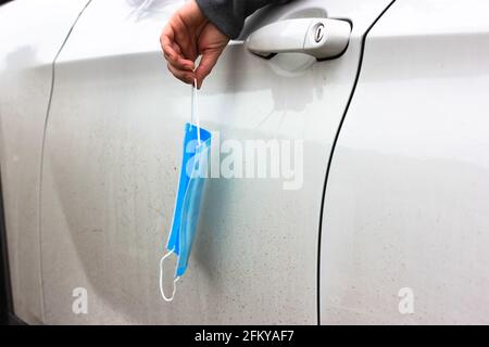 Un conducteur d'une voiture blanche jette un masque médical usagé par la fenêtre, mettre fin à la pandémie. Banque D'Images