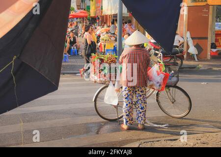 Hanoi, Vietnam - Mars 10 2019: Un vendeur local de rue vietnamienne vend des fruits de l'arrière de sa bicyclette, portant un traditionnel conique non la chapeau dedans Banque D'Images