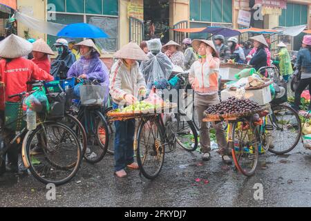 Hanoï, Vietnam - février 28 2019 : les vendeurs locaux de rue vietnamiens vendent des fruits à partir de l'arrière de leurs vélos lors d'un jour pluvieux dans la ville animée de stre Banque D'Images