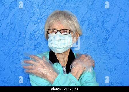 Une femme âgée croise ses bras de manière protective dans tout son corps. Craignant d'attraper le virus Covid 19, elle porte un masque et des gants et est debout Banque D'Images