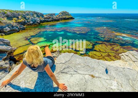 Une jeune fille touristique caucasienne fait du soleil sur des rochers qui regardent les eaux turquoise de Jeannies Lookout à Rottnest Island, Perth, Australie occidentale. Vue panoramique Banque D'Images