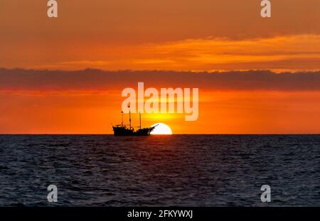 Un Pirate Ship se trouve sur l'océan, détouré contre UN Ciel coloré de coucher de soleil orange Banque D'Images