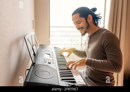 Jeune latino-américain apprenant à jouer du piano à la maison pendant quarantaine Banque D'Images