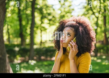 Jolie femme afro parlant sur le téléphone portable dans l'étonnement, dans un jardin. Banque D'Images