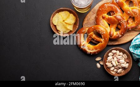 Tasse à bière lager, noix, chips de pomme de terre et bretzel maison frais cuit avec sel de mer sur table en pierre. Collation classique à la bière. Vue de dessus plat avec bac à papier Banque D'Images