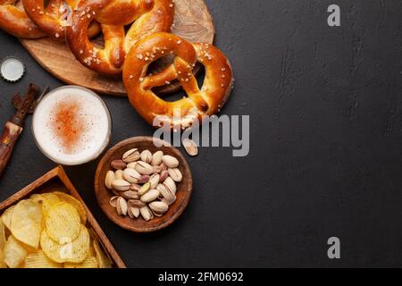 Tasse à bière lager, noix, chips de pomme de terre et bretzel maison frais cuit avec sel de mer sur table en pierre. Collation classique à la bière. Vue de dessus plat avec bac à papier Banque D'Images