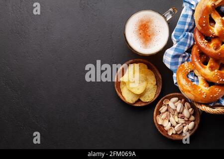 Tasse à bière lager, noix, chips de pomme de terre et bretzel maison frais cuit avec sel de mer sur table en pierre. Collation classique à la bière. Vue de dessus plat avec bac à papier Banque D'Images