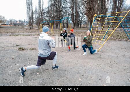 Cours de fitness en groupe à l'extérieur. Cours d'entraînement en plein air socialement distants dans les parcs publics. Trois femmes et l'homme s'entraîner ensemble dans le public Banque D'Images