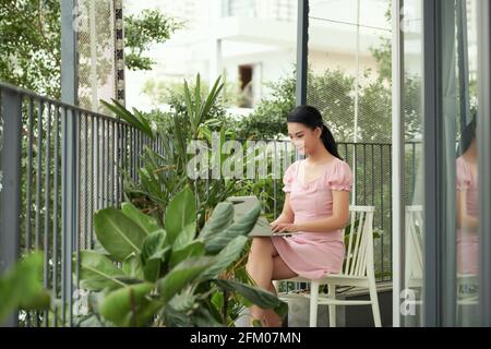Jeune femme indépendante travaillant sur un ordinateur portable assis à une table sur le balcon Banque D'Images