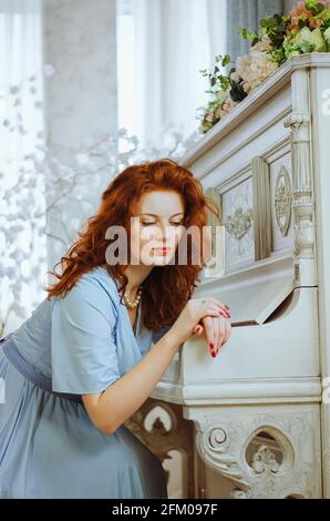 Belle jeune pianiste aux cheveux rouges avec des yeux bleus et des freckles assis près d'un piano et de la musique d'apprentissage en studio. Le processus créatif de faire Banque D'Images