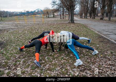 Cours de fitness en groupe à l'extérieur. Cours d'entraînement en plein air socialement distants dans les parcs publics. Trois femmes et l'homme s'entraîner ensemble dans le public Banque D'Images