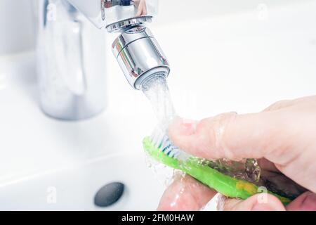 Nettoyage D'UNE brosse à dents sous l'eau qui coule dans l'évier de la salle de bains Banque D'Images