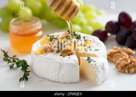 Miel versé sur le camembert avec des noix et des raisins. Hors-d'œuvre au fromage gastronomique brie ou camembert avec miel, noix, fruits Banque D'Images