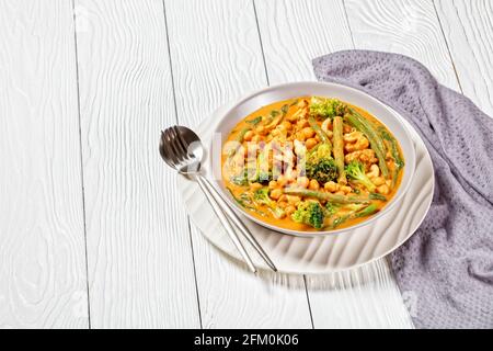 curry de noix de coco végétarien avec pois chiches, haricots verts, chou-fleur et brocolis dans un bol sur une table en bois blanc, cuisine indienne Banque D'Images