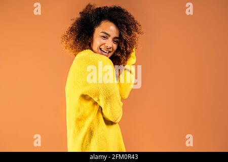 Jeune femme noire gaie souriant et regardant l'appareil photo en studio tourné sur fond marron. Banque D'Images