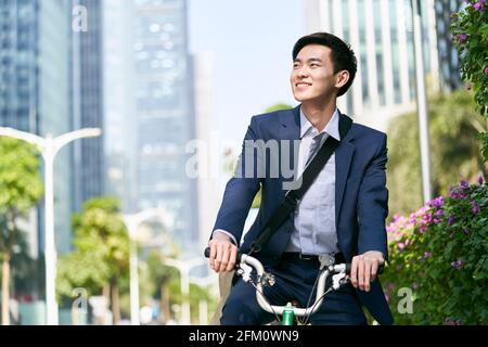 jeune homme d'affaires asiatique à vélo dans le quartier financier du centre-ville de la ville moderne, heureux et souriant Banque D'Images