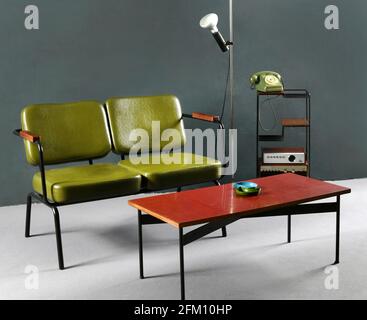 La 70ème table et le canapé vintage sont placés près de la lampe et de la tablette avec téléphone et radio dans la chambre avec mur gris et sol Banque D'Images