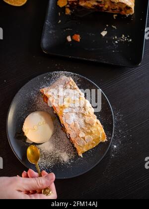 Délicieux strudel frais farci de pommes et de raisins secs, servi avec une boule de glace, un magnifique dessert, fond noir, vue de dessus. Banque D'Images