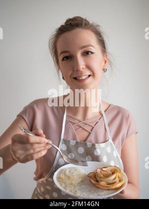 Le chef cuisinier féminin heureux tient une assiette de roses de pomme préparée par elle-même. Banque D'Images