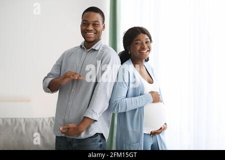 Homme noir aimant imitant sa femme enceinte et souriant Banque D'Images