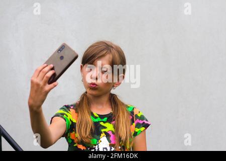 Mise au point automatique. Préteen fille pose et prend un selfie. Petite fille gaiFull prenant une photo avec un smartphone. Fond gris blanc. Sourire Banque D'Images