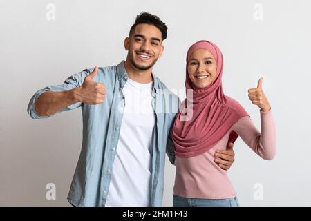 Heureux couple musulman du millénaire qui s'embrasse et montre Thumbs Up à Appareil photo Banque D'Images