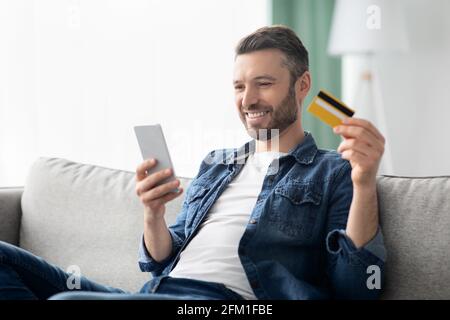 Homme positif avec smartphone tenant la carte de crédit Banque D'Images