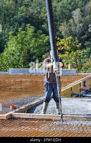 Verser le béton dans le treillis d'armature pour les sols. Processus de mise en place d'une nouvelle maison. Ouvrier de construction tenant le tuyau de la machine à pompe tout en concrétisant les plafonds. Banque D'Images