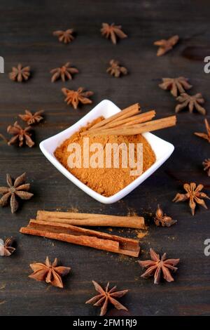 Bol de poudre de cannelle moulue et bâtonnets avec anis étoilé éparpillées sur une table en bois noir Banque D'Images