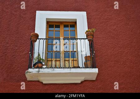 Maison coloniale espagnole avec un mur en stuc rouge vénitien, fenêtre en pierre et un balcon en fer forgé avec des balustrades en argile à Guanajuato, Mexique. Banque D'Images