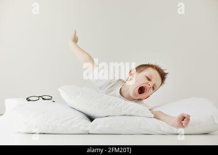 Enfant garçon se réveille et s'étire sur son lit confortable le matin, les soins de santé et le concept du monde du matin. Étirements et yawns Banque D'Images