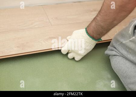Installation d'un sol stratifié ou de parquet dans la pièce, détails sur les mains de l'homme portant des carreaux de bois, sur la base en mousse verte. Banque D'Images