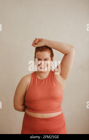 Portrait d'une femme belle et saine dans les vêtements de sport. Femme de taille plus regardant l'appareil photo et souriant au studio de fitness. Banque D'Images