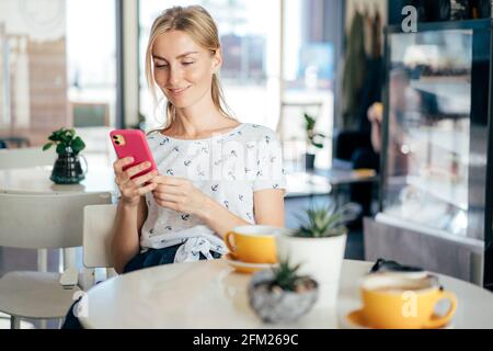 Une jeune femme prend le petit déjeuner dans un café. La jeune fille est en train de discuter sur Internet sur un téléphone mobile. Une femme attrayante utilise la technologie Wi-fi sans fil. S Banque D'Images