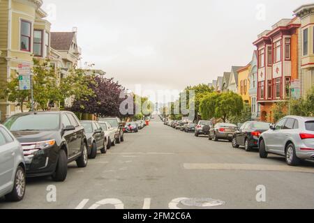 Photo horizontale d'une belle route avec des arbres, des voitures garées et des maisons traditionnelles de San Francisco des deux côtés, Californie - États-Unis d'Amérique Banque D'Images