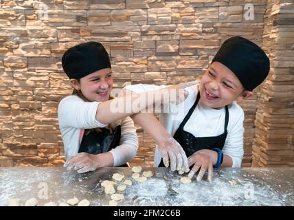 Garçons et filles frères et sœurs jumeaux jouant tout en cuisant avec de la farine dans les tenues du chef Banque D'Images