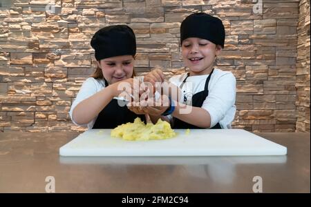 Garçon et fille qui dépose un œuf dans une pâte de pommes de terre tout en faisant un atelier de cuisine. Les enfants cuisent Banque D'Images