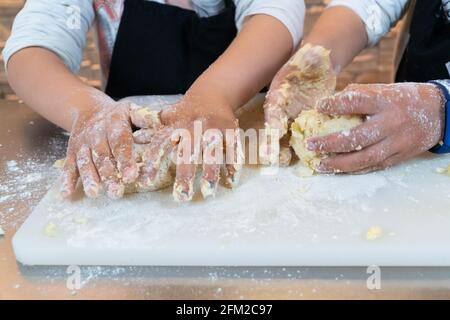 Enfants méconnaissables pétrissant une boule de pâte dans une cuisine atelier dans les vêtements du chef Banque D'Images