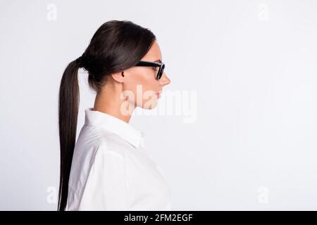 Photo de profil de la femme optimiste brunette hairdo près de l'espace vide porter des lunettes blanc chemise isolée sur fond gris Banque D'Images